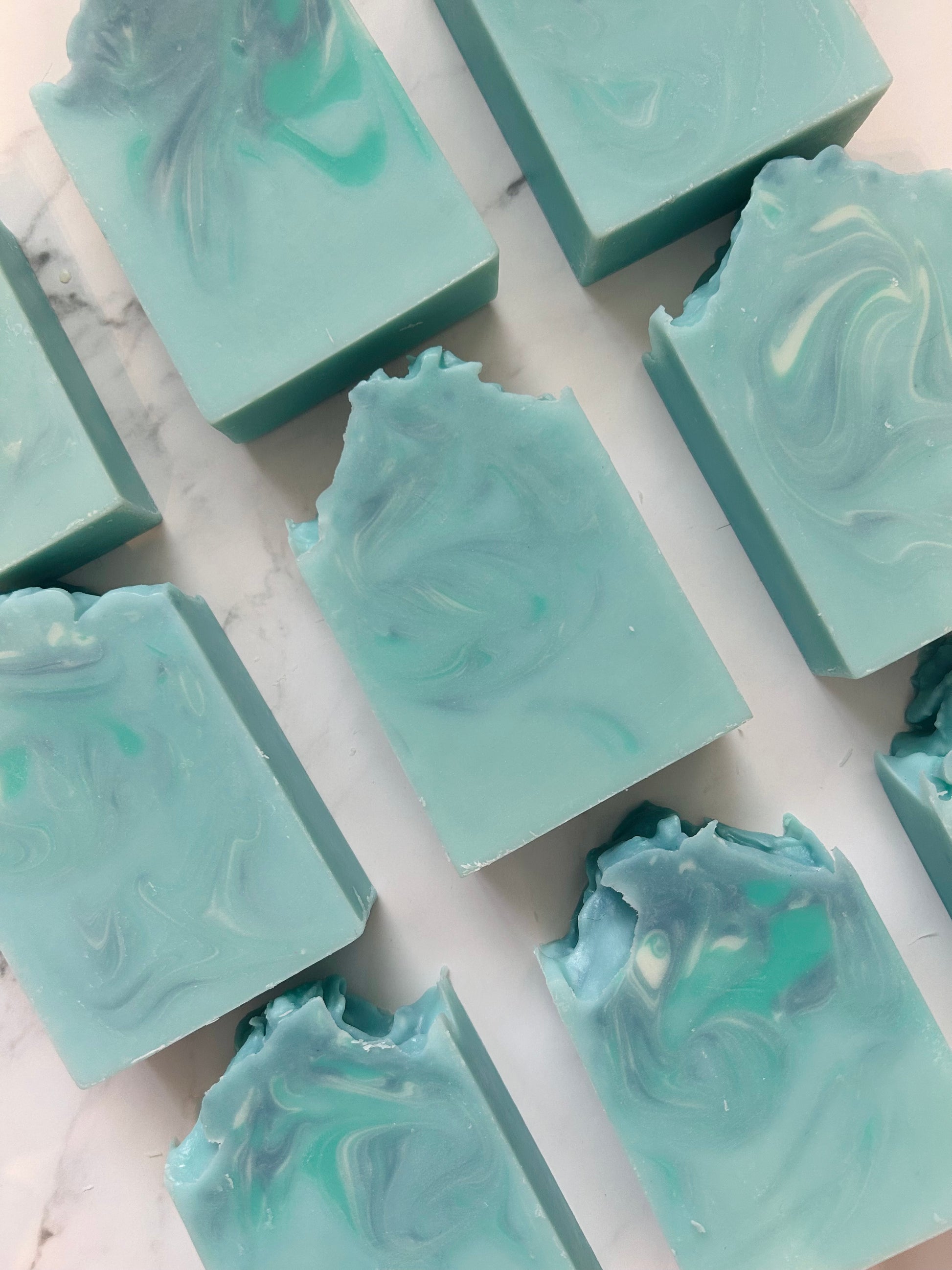 Image of 9 blue, white, and teal swirled soap bars photographed vertically on a white marble background.