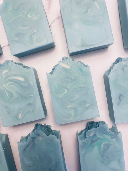 Image of 9 blue, white, and green swirled soap bars photographed vertically on a white marbled background.