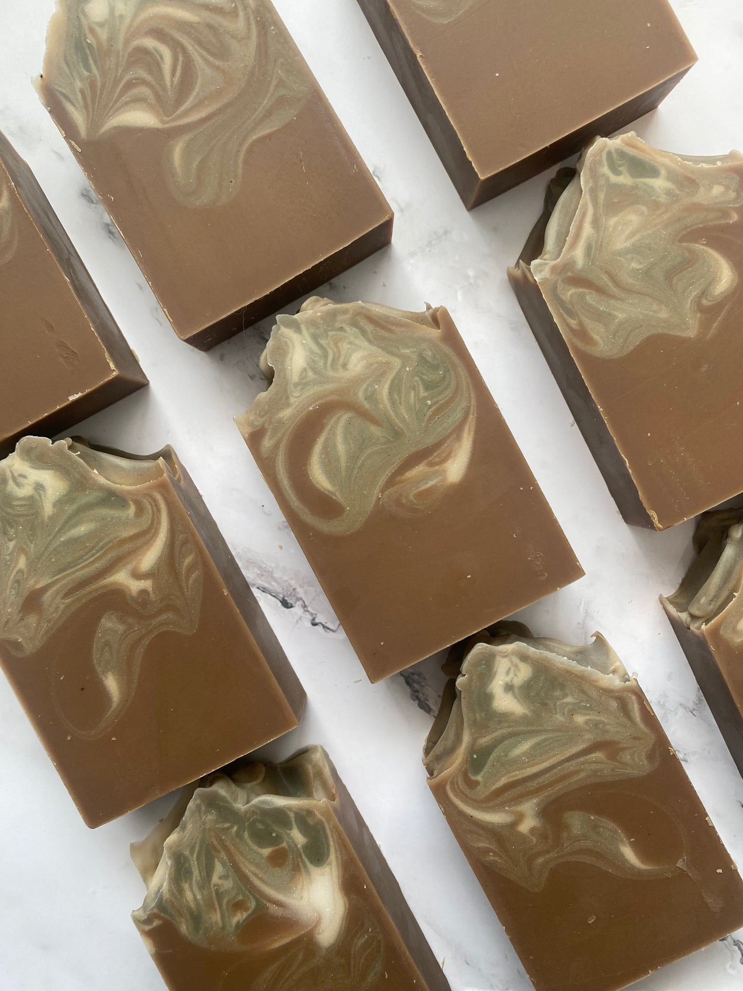 Image of 9 brown, white, and gray swirled soap bars photographed vertically on a white marble background.