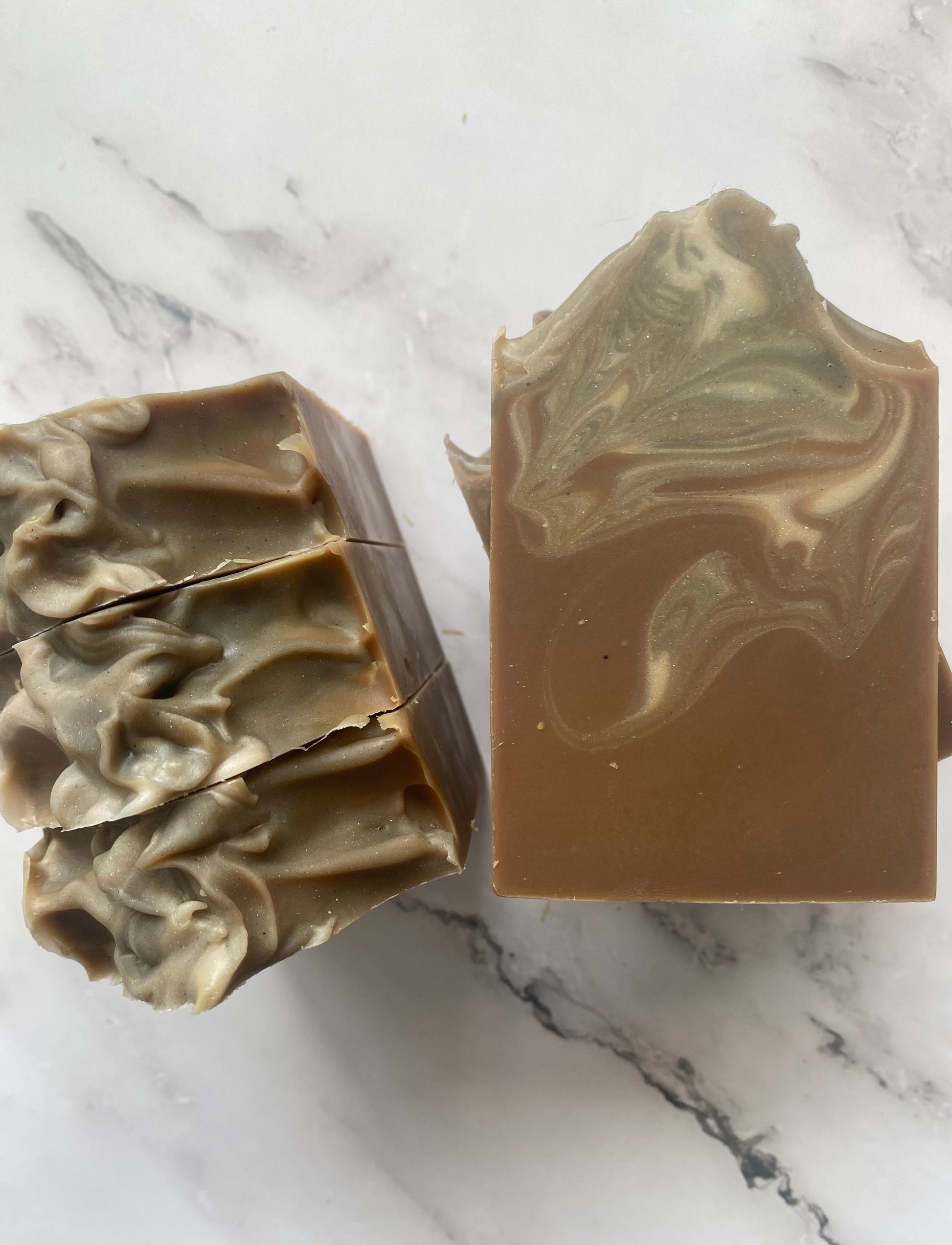 Image of brown, white, and gray swirled soap bars with 3 bars stacked on top of one another and 3 bars standing vertically photographed on a white marble background.