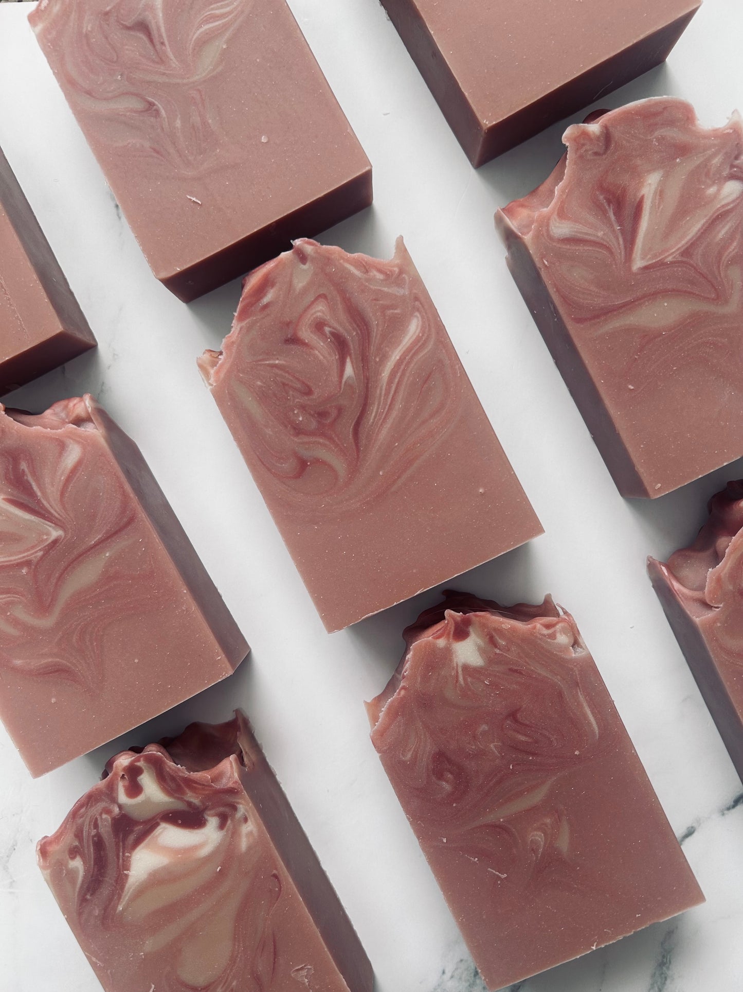 Image of 9 dusty mauve and white swirled soap bars photographed vertically on a white marble background.