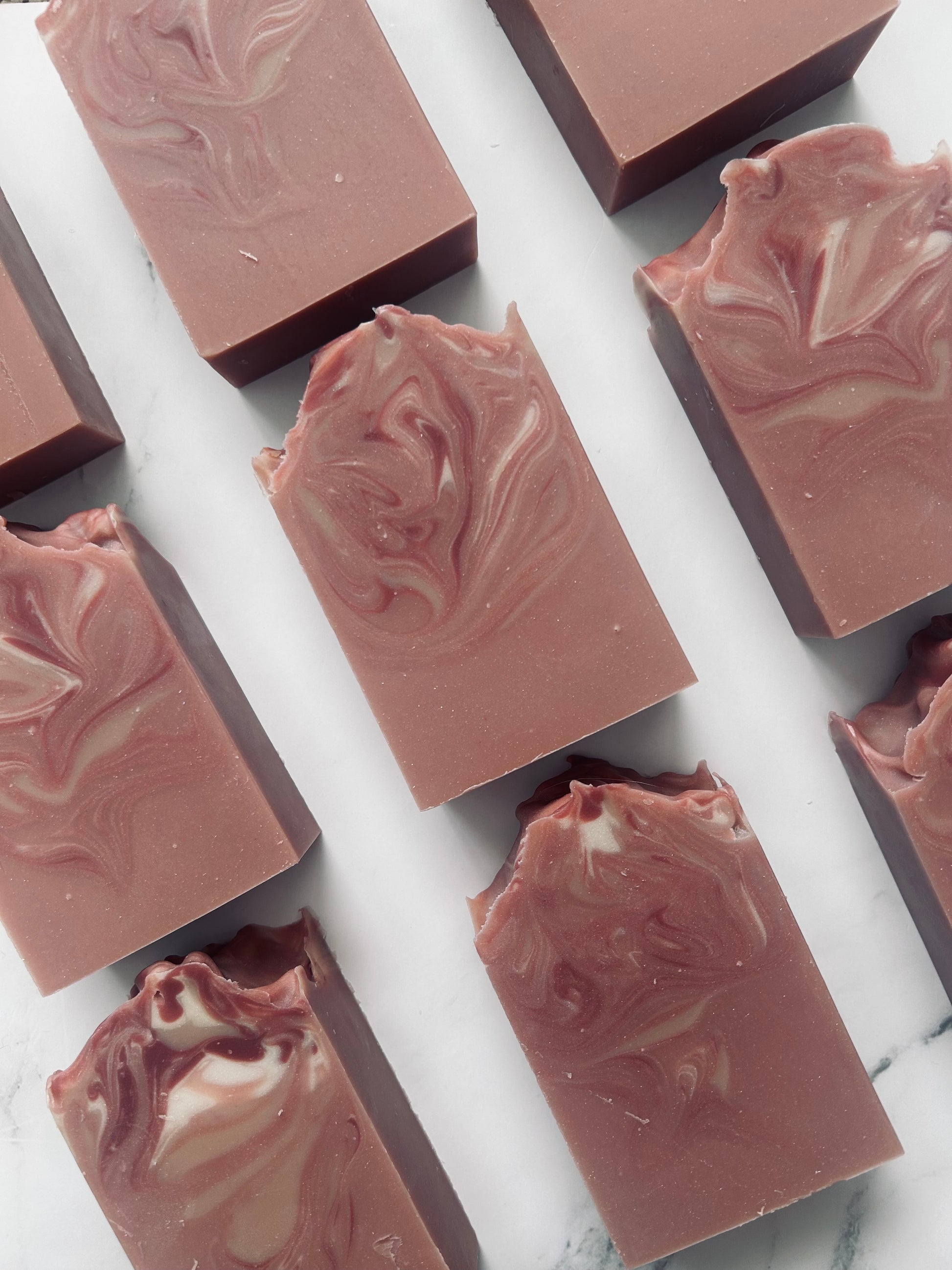 Image of 9 dusty mauve and white swirled soap bars photographed vertically on a white marble background.