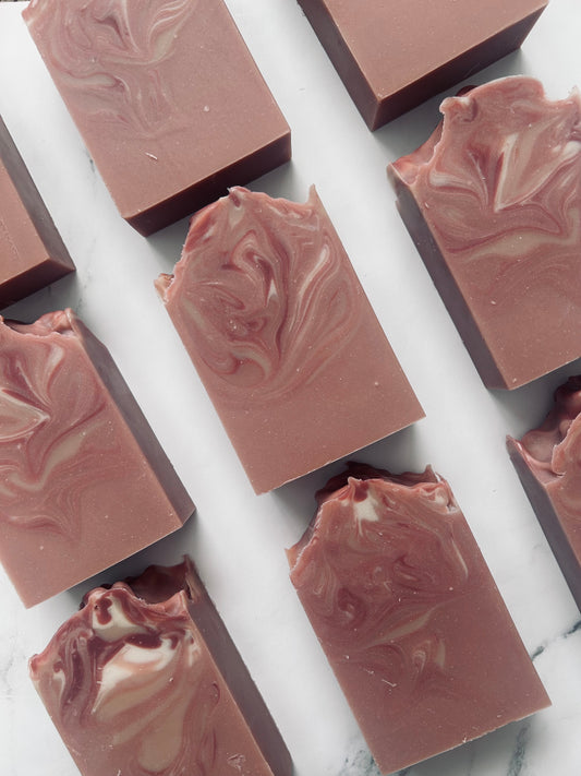 Image of 9 dusty mauve and white swirled soap bars photographed vertically on a white marble background.
