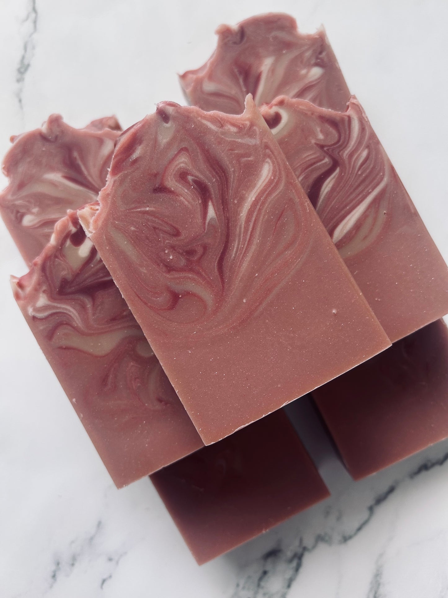 Image of 7 dusty mauve and white swirled soap bars stacked on top of one another photographed on a white marble background.