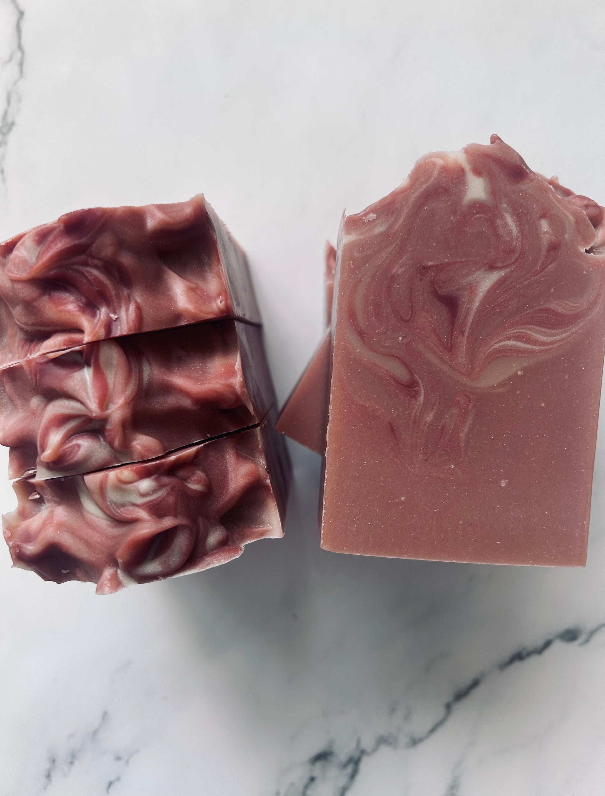 Image of dusty mauve  and white swirled soap bars with 3 bars stacked on top of one another and 3 bars standing vertically photographed on a white marble background.